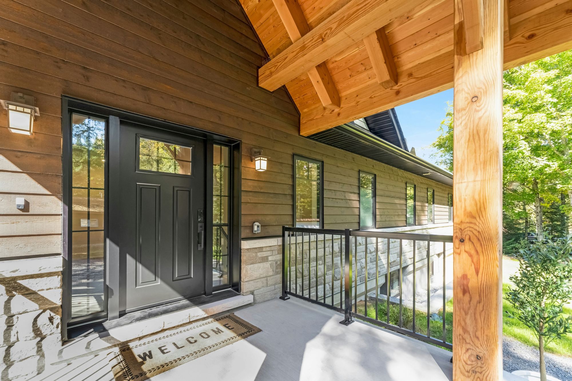 Porte d'entrée noire avec vitrages latéraux sur une façade en bois